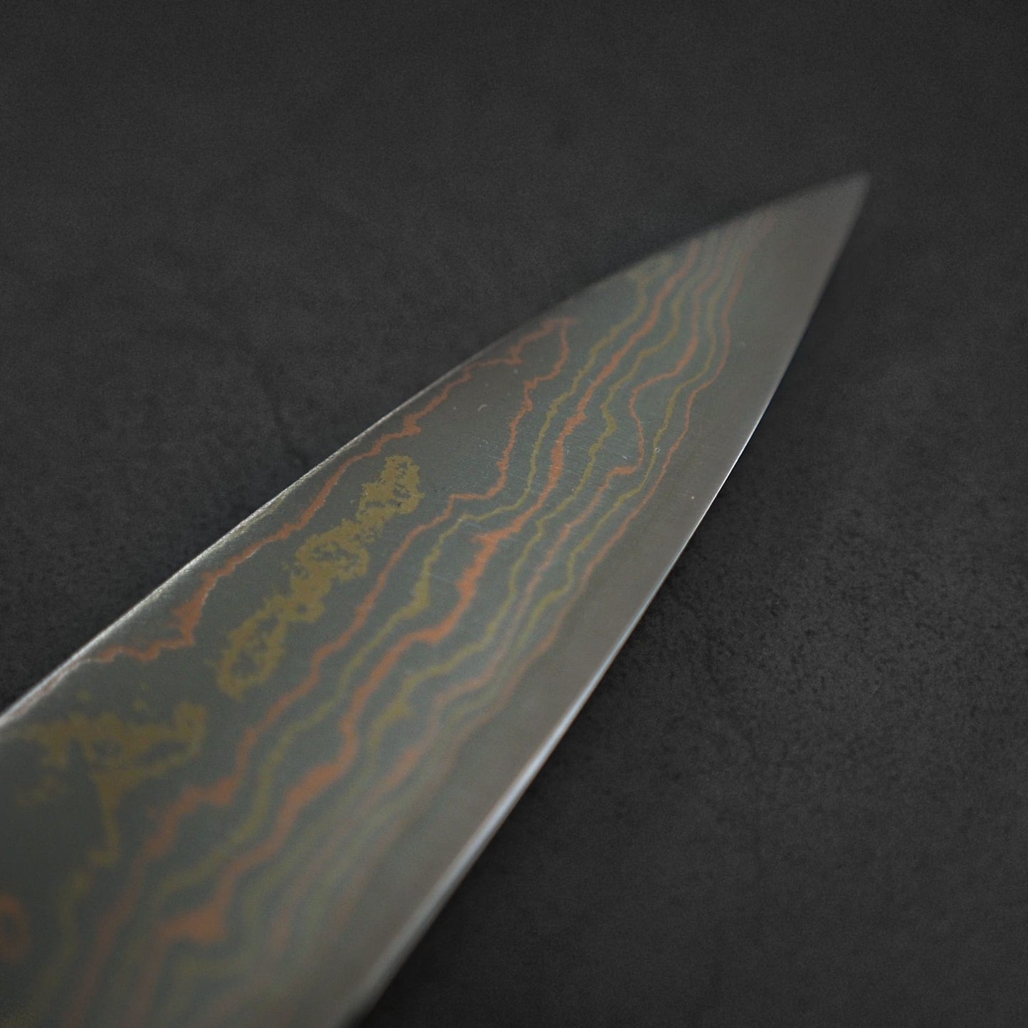 Close-up of the Takeshi Saji Rainbow Damascus Aogami#2 Gyuto 210mm blade, showcasing its striking Damascus pattern and distinctive craftsmanship against a dark background.