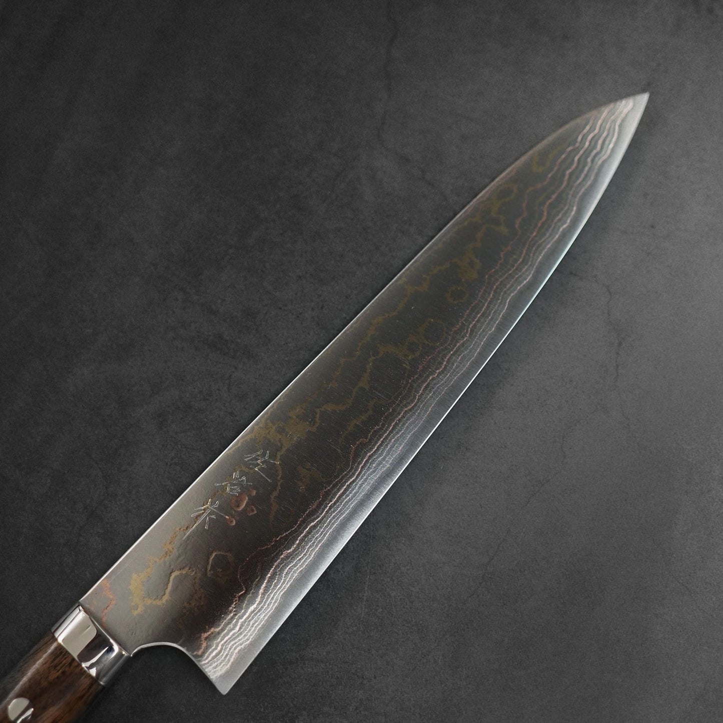 The Takeshi Saji rainbow damascus aogami#2 gyuto 240mm features a wooden handle and a Damascus steel blade with striking wavy patterns, crafted by Takeshi Saji from premium aogami#2 steel, and displayed on a dark textured background.
