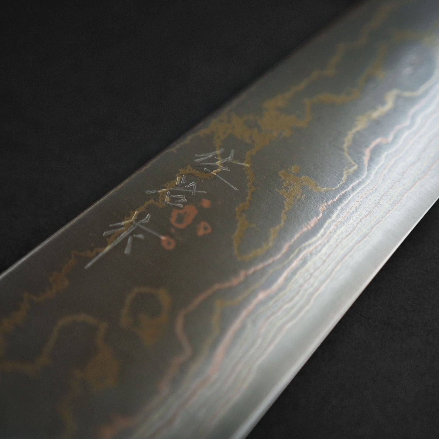 Close-up of the Takeshi Saji rainbow damascus aogami#2 gyuto 240mm, highlighting its layered blade, striking hamon patterns, and engraved kanji characters on a dark background.