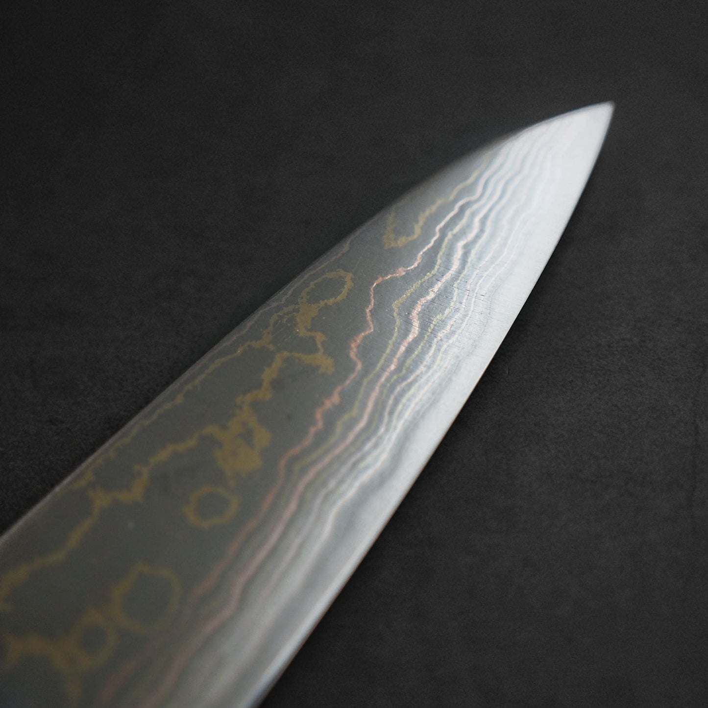 Close-up of a Takeshi Saji Rainbow Damascus Aogami#2 Gyuto 240mm blade, showcasing its striking wavy pattern against a dark background.