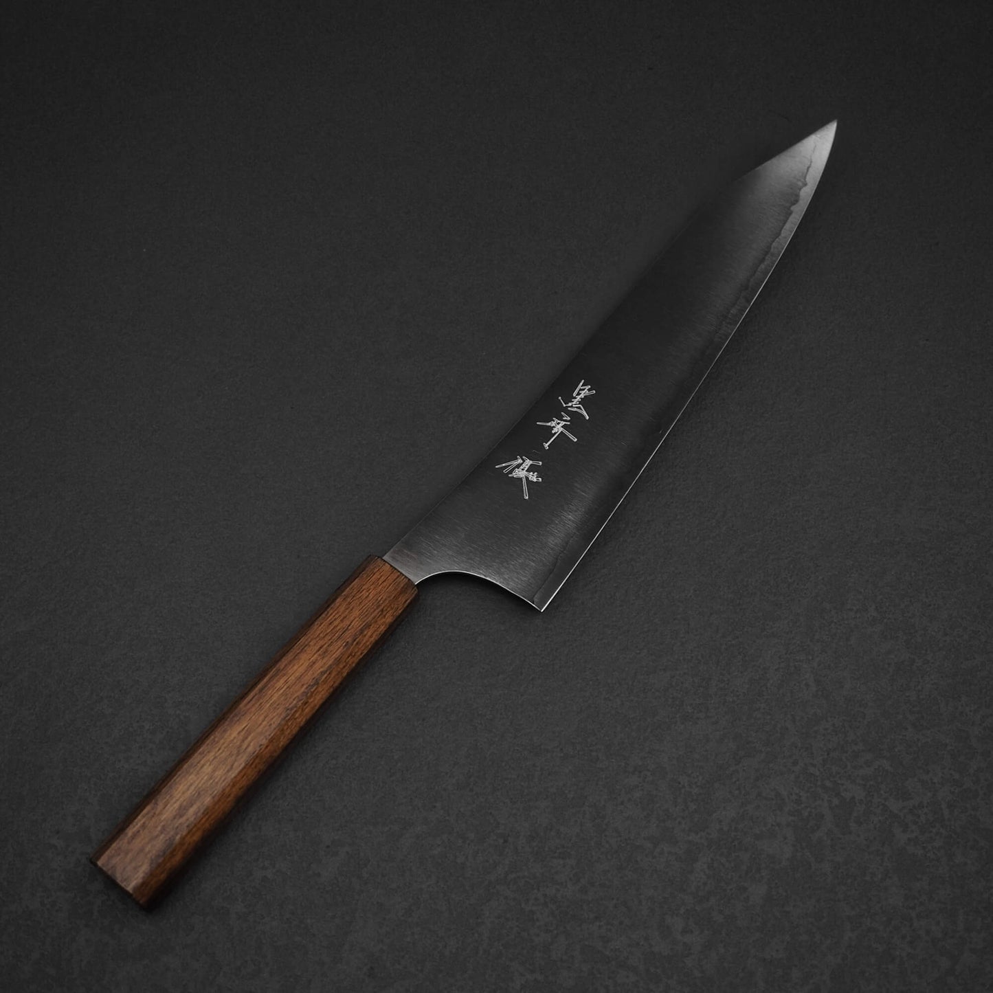 The Yu Kurosaki HAP40 Gekko kiritsuke gyuto 210mm kitchen knife features a dark wooden handle and razor-sharp HAP40 steel blade with kanji engravings, displayed on a dark textured surface.