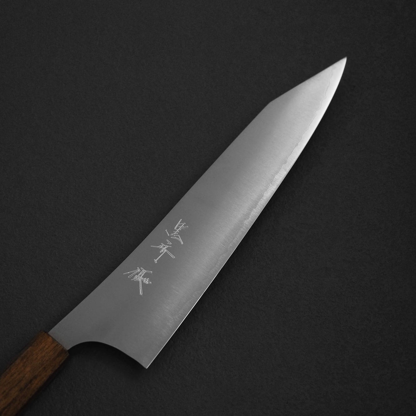 The Yu Kurosaki HAP40 Gekko kiritsuke gyuto 210mm chef’s knife features a wooden handle and engraved HAP40 steel blade, displayed elegantly on a dark surface.