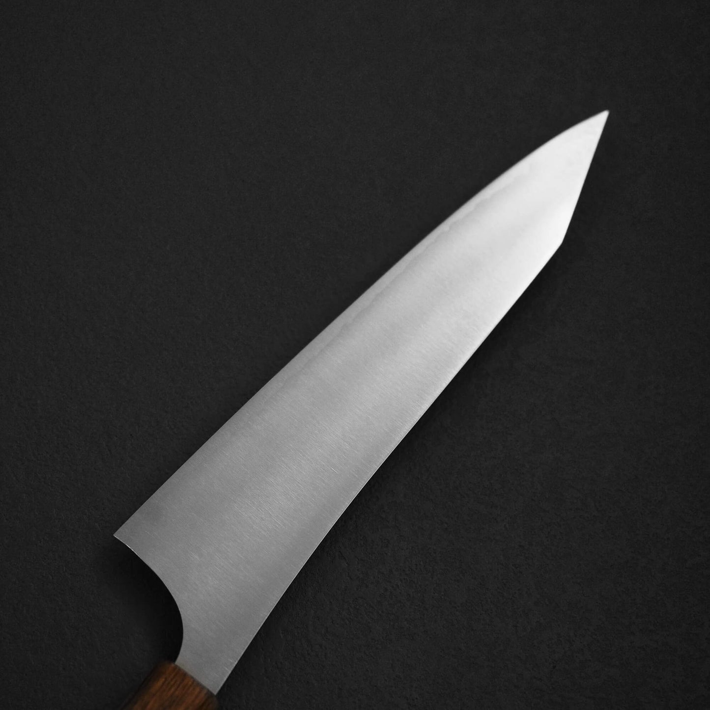 A close-up of the Yu Kurosaki HAP40 Gekko kiritsuke gyuto 210mm kitchen knife with a sharp HAP40 steel blade and wooden handle, set against a dark, textured background.