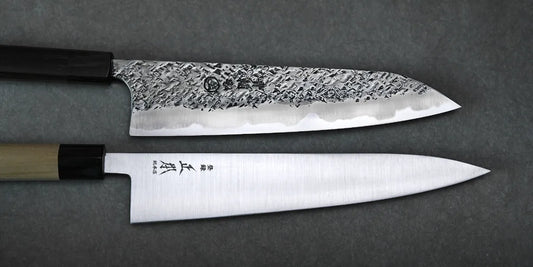 A carbon steel and a stainless steel gyuto knife against a dark grey background