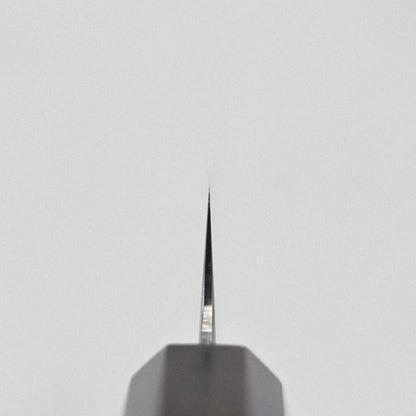 Close-up of sujihiki tip, pointed upward; blade’s profile and grind are clearly visible.