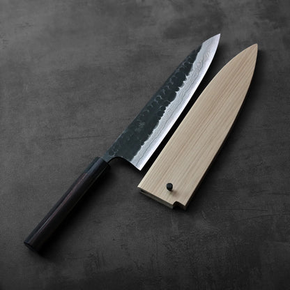 Gyuto with a dark handle and a custom magnolia saya, highlighting its distinctive protective cover.
