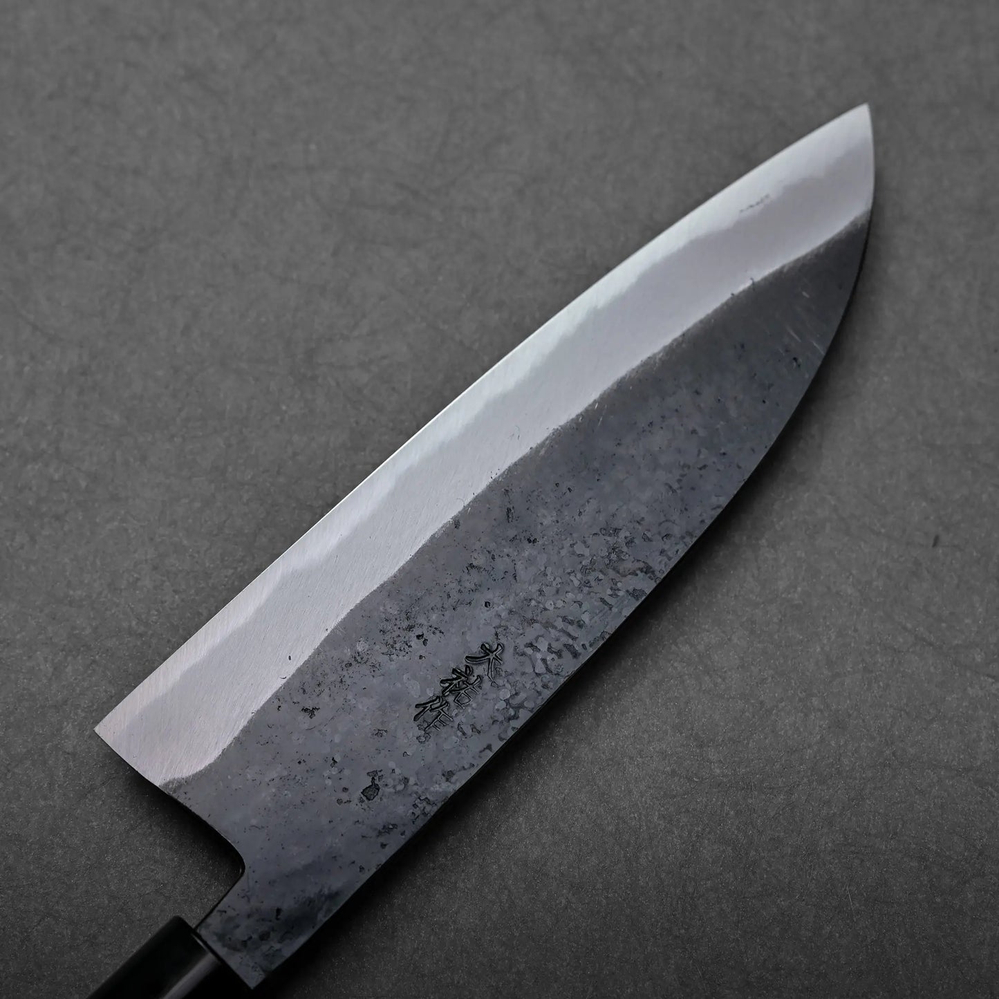 A santoku blade with a dark, textured finish is shown; a Japanese knife featuring a broad, rounded tip.
