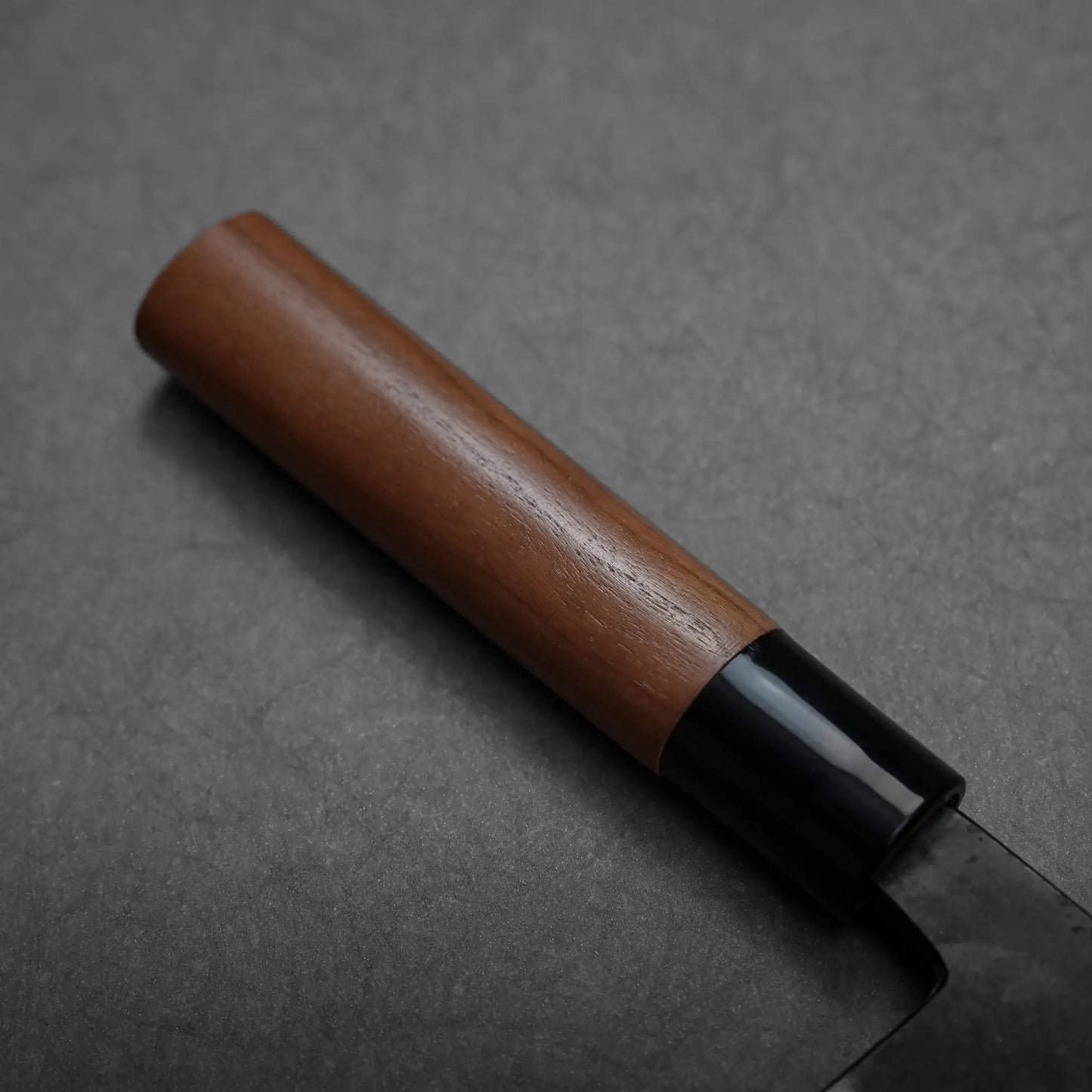 Close-up shows the blade finish and wooden handle of a Japanese knife by Daisuke Nishida, blade shape not fully visible.
