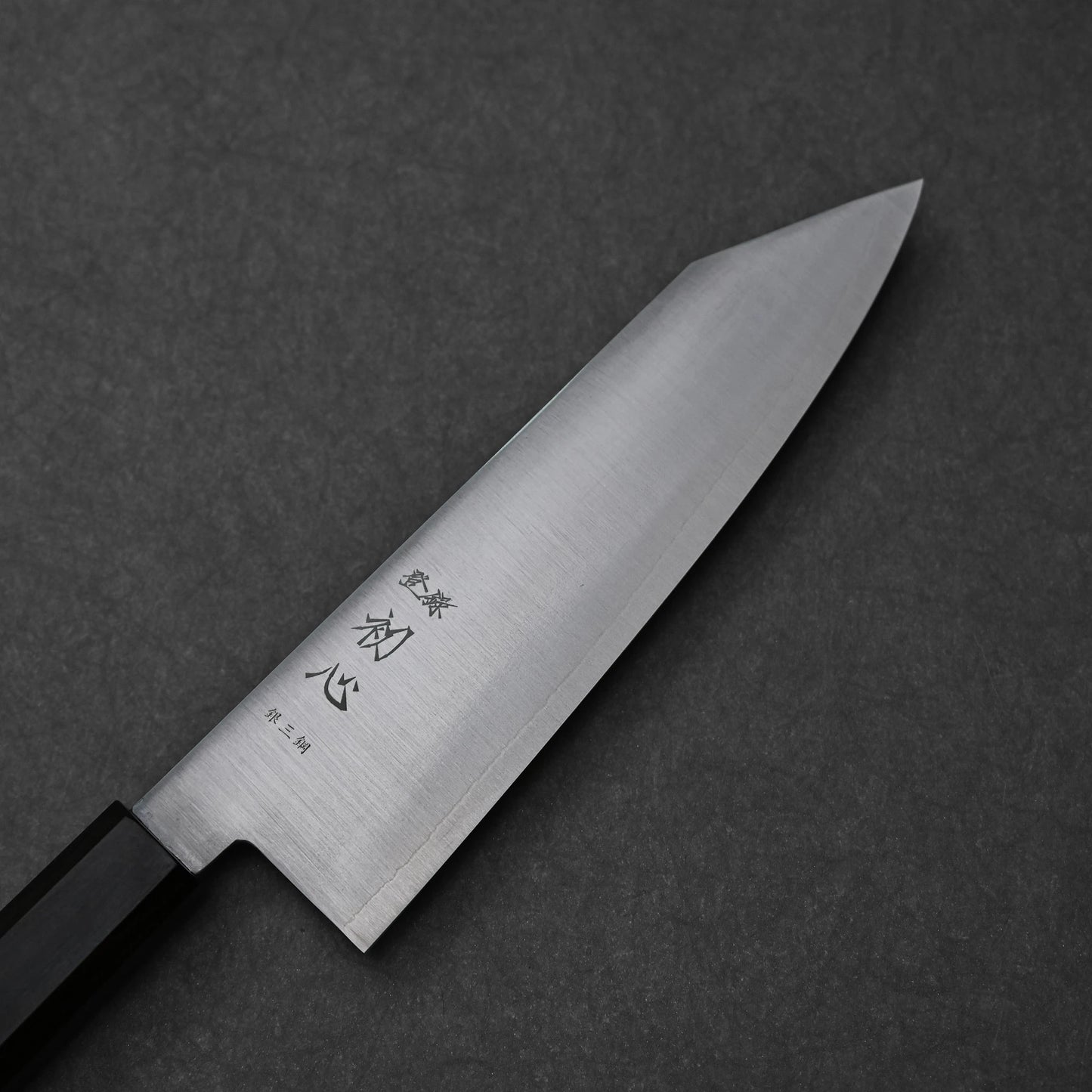 Close-up of a bunka knife made with ginsan stainless steel; photographed to highlight the pointed tip, vertically engraved kanji characters, and polished steel surface.