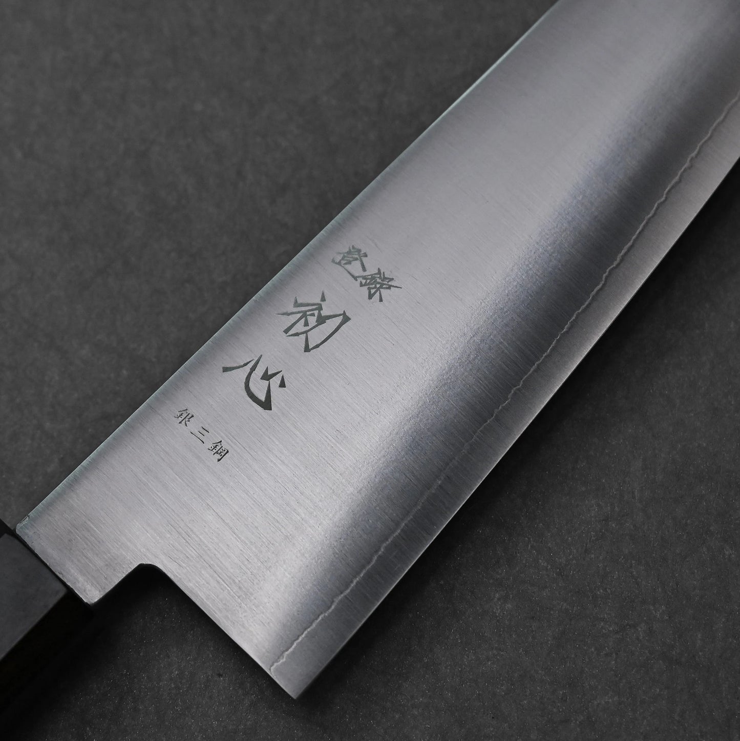 Close-up of a bunka knife made with ginsan stainless steel; photographed to highlight vertically engraved kanji characters and the polished steel finish.
