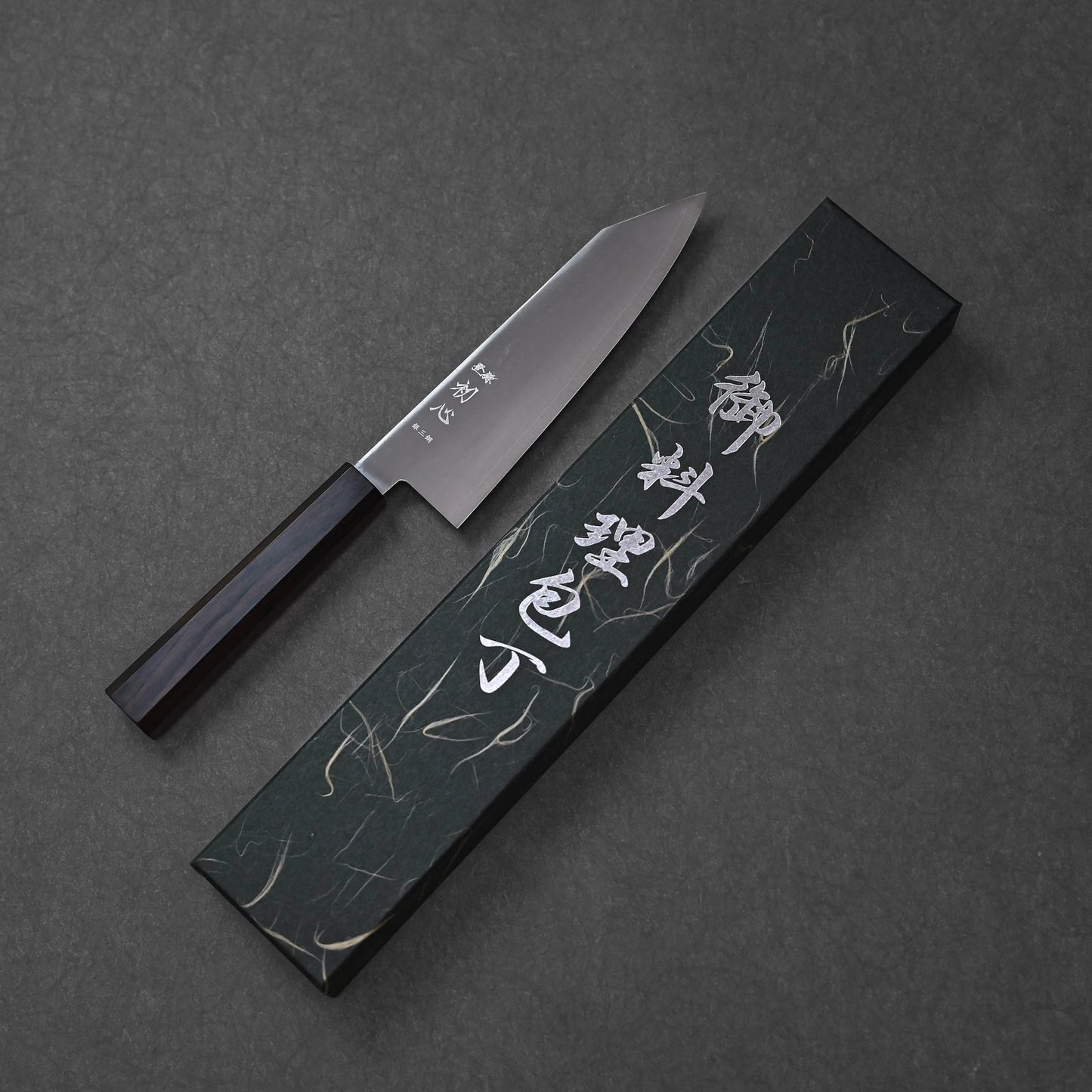 Bunka knife made with ginsan stainless steel, presented alongside its matching box; photographed to highlight the full blade profile, dark octagonal handle, and the patterned black box with white Japanese characters.