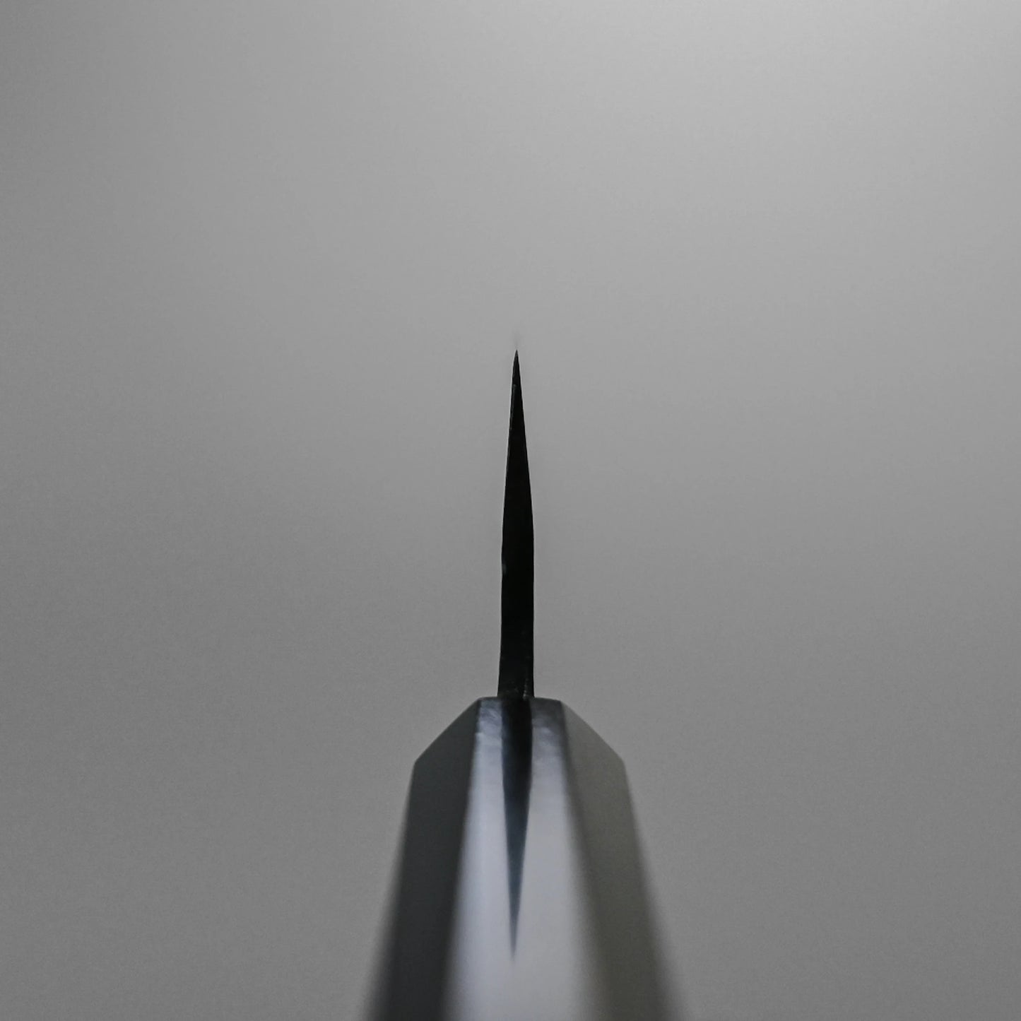 Choil shot of the Hatsukokoro Kurouchi Aogami#2 Ko-Bunka 120mm knife tip, centered against a plain light gray background. The blade displays Hatsukokoro’s signature kurouchi finish and is crafted from premium Aogami #2 steel.