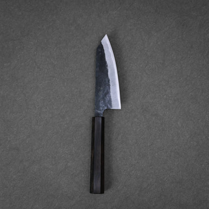A Hatsukokoro kurouchi aogami#2 ko-bunka 120mm kitchen knife with a dark wooden handle and wide, slightly curved blade rests on a textured gray surface.
