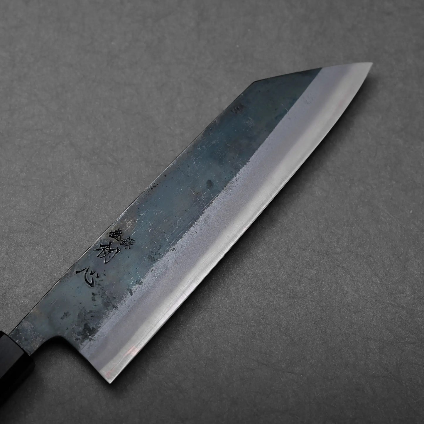 A black-handled Japanese knife, identifiable as a kiritsuke gyuto, features an angled blade with a flat edge.