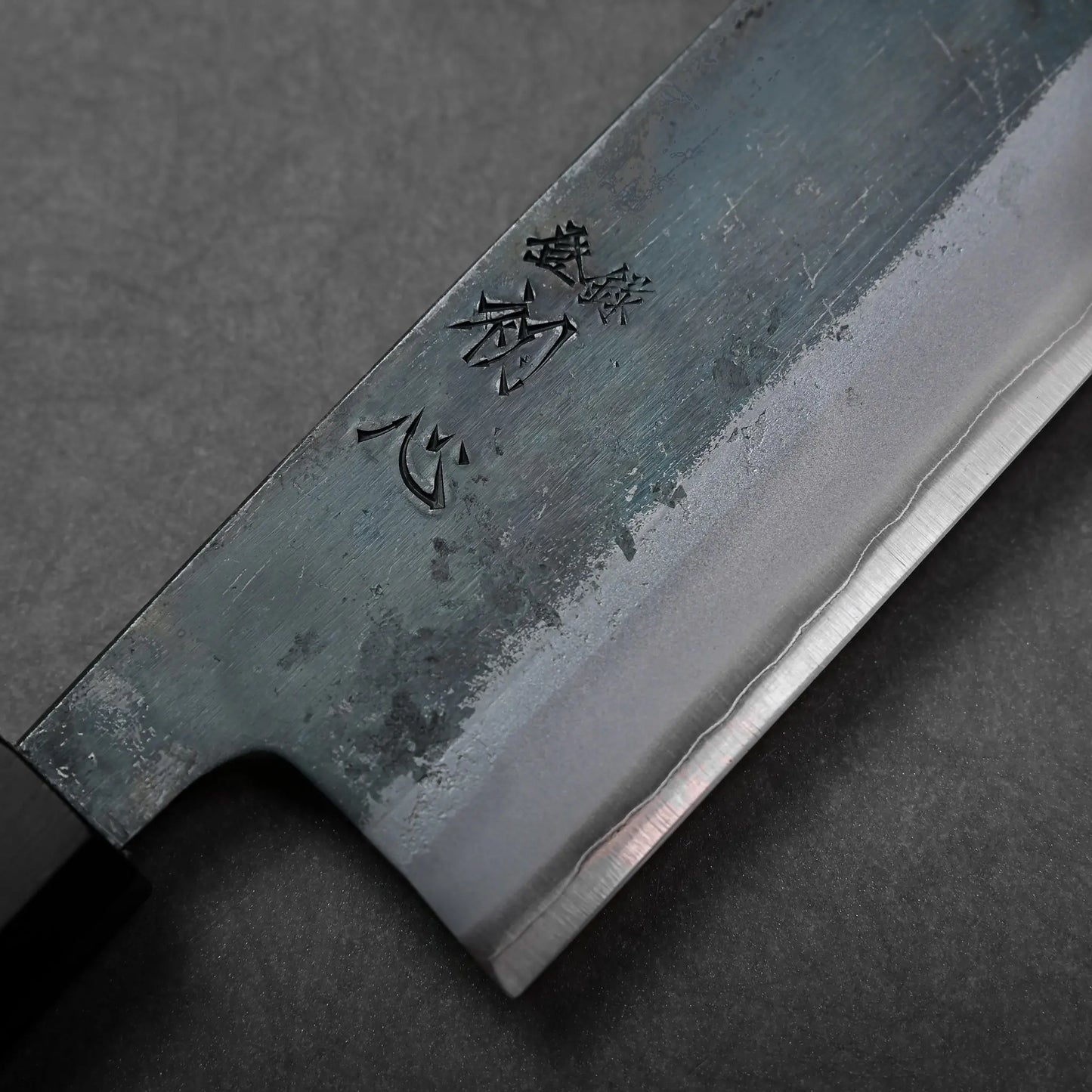 Blade close-up showing kanji engravings on a Japanese knife, with visible kiritsuke gyuto shape and straight edge.