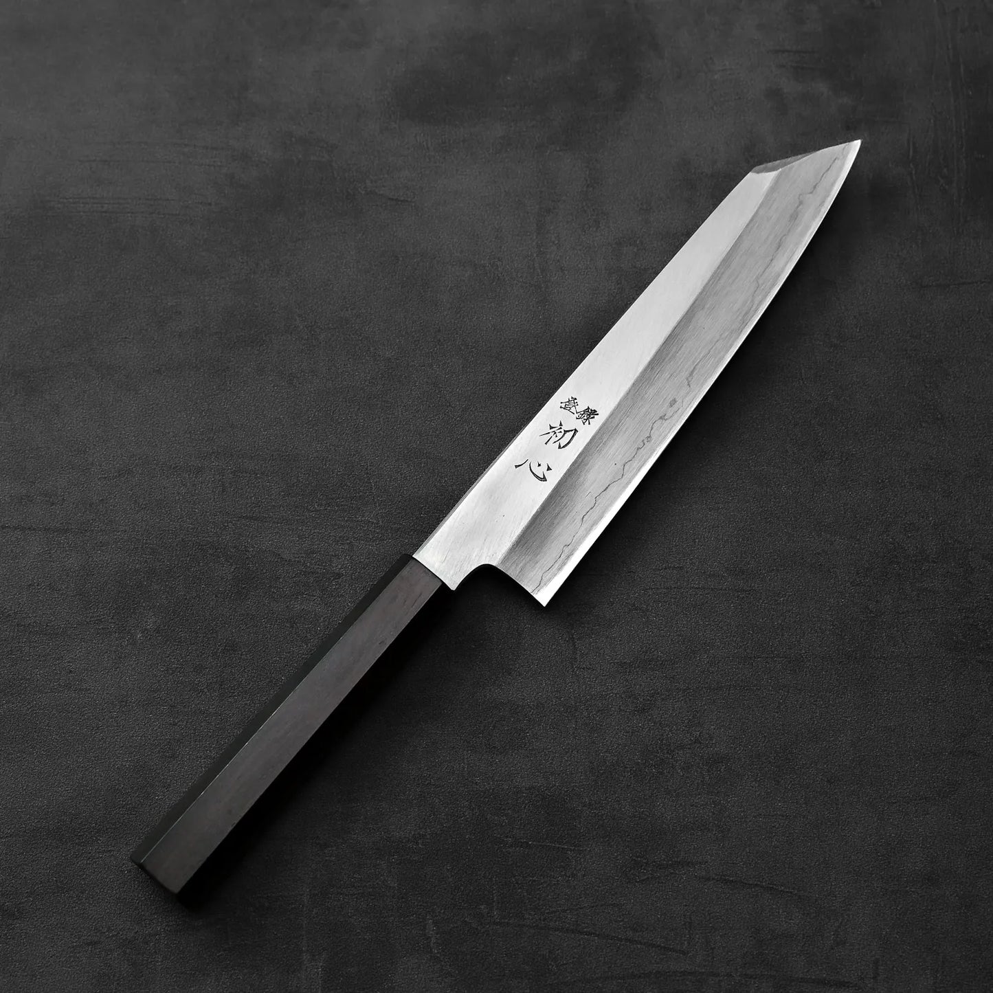 Hatsukokoro x Nakagawa ginsan kiritsuke gyuto 210mm with a black handle is shown, highlighting its distinct silhouette and smooth lines.