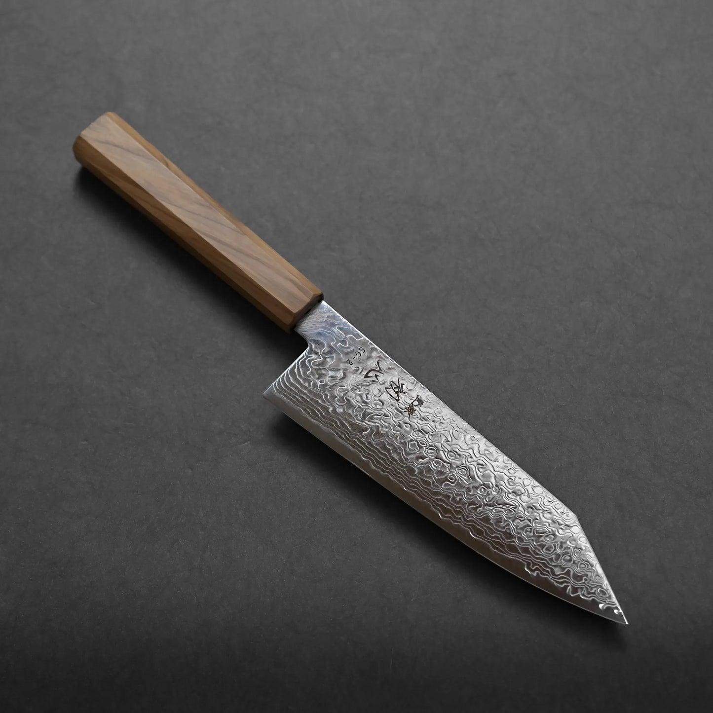 A Japanese-style chef's knife with a beautiful Damascus steel blade and a wooden handle rests on a dark gray surface.