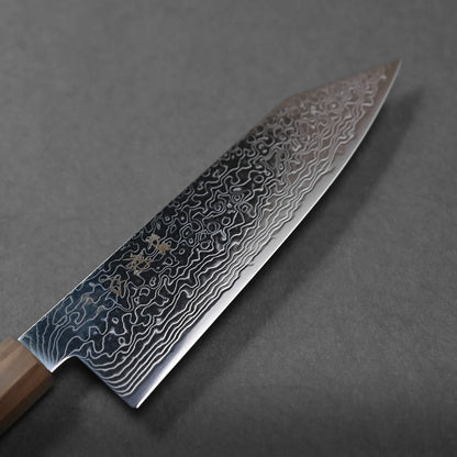 A close-up of a Japanese chef’s knife with a wooden handle, showcasing a patterned Damascus steel blade resting on a dark gray surface.