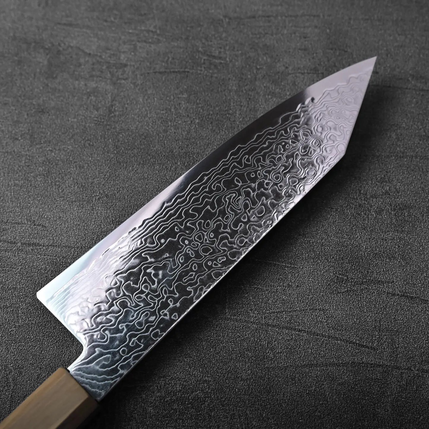 Close-up of a bunka knife with a patterned blade and a visible spine, captured in clear detail.