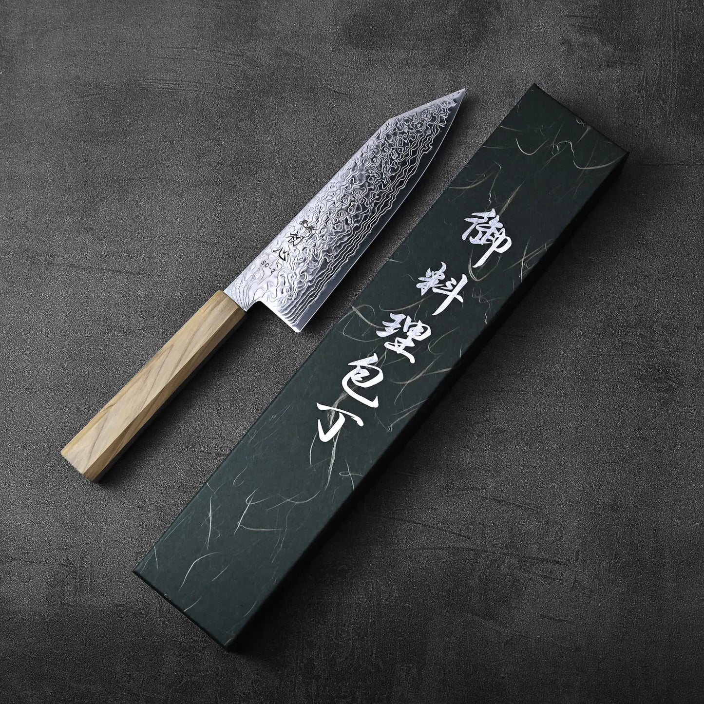 Bunka with a wooden handle next to a black box featuring white Japanese characters.