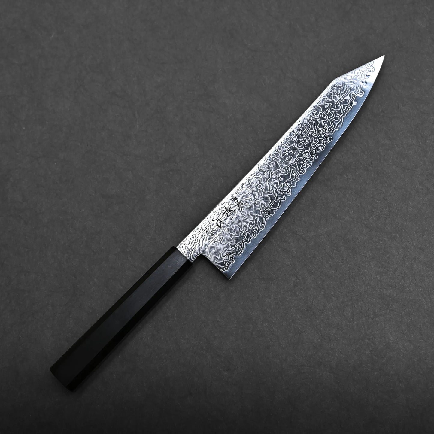 A Hatsukokoro Ryuhyo SG2 damascus kiritsuke gyuto 210mm with a black handle and a patterned, Damascus steel blade is displayed on a dark, textured background.
