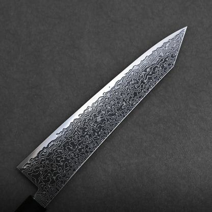 A close-up of a ktip gyuto chef’s knife with a patterned Damascus steel blade, showing intricate wavy designs, set against a dark textured background.