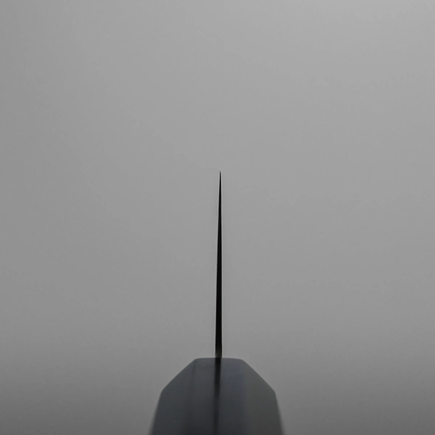 Choil shot of a ktip gyuto against a plain grey background, emphasizing the sharpness and symmetry of the blade.