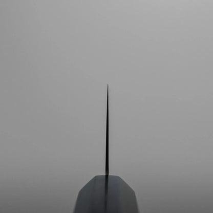 Choil shot of a ktip gyuto against a plain grey background, emphasizing the sharpness and symmetry of the blade.