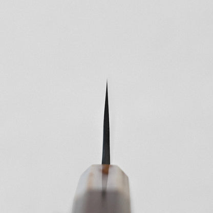 Close-up of a gyuto with its tip pointing upward, showing damascus pattern and kurouchi finish.
