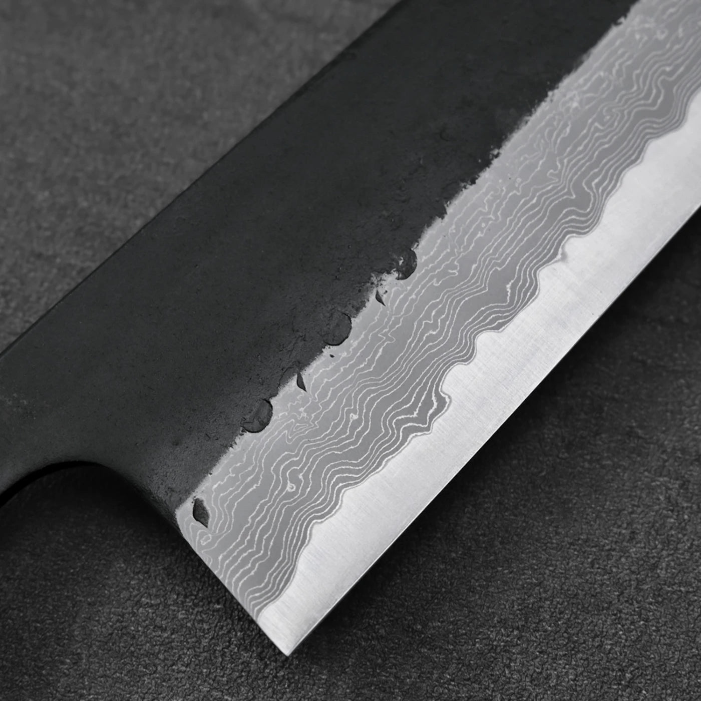 Gyuto with a close-up view of wavy Damascus steel patterns across the blade, highlighting its texture.