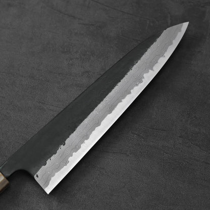 A gyuto with a kurouchi damascus finish is shown resting in a horizontal position.