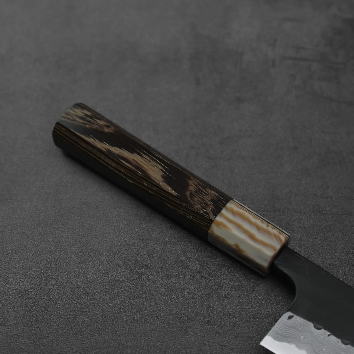 Close-up of gyuto handle featuring kurouchi damascus finish and AS steel, shown in detailed focus.