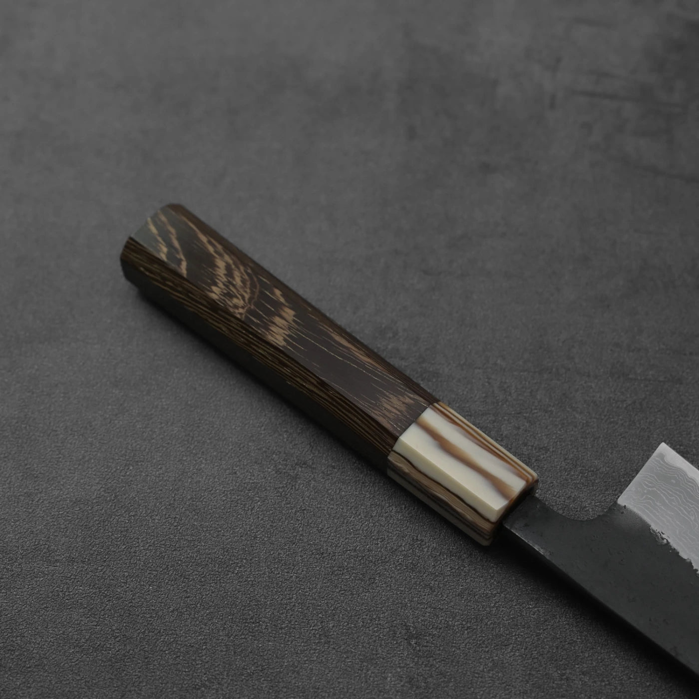 Close-up of a gyuto featuring kurouchi damascus pattern and AS steel, focusing on blade detail.