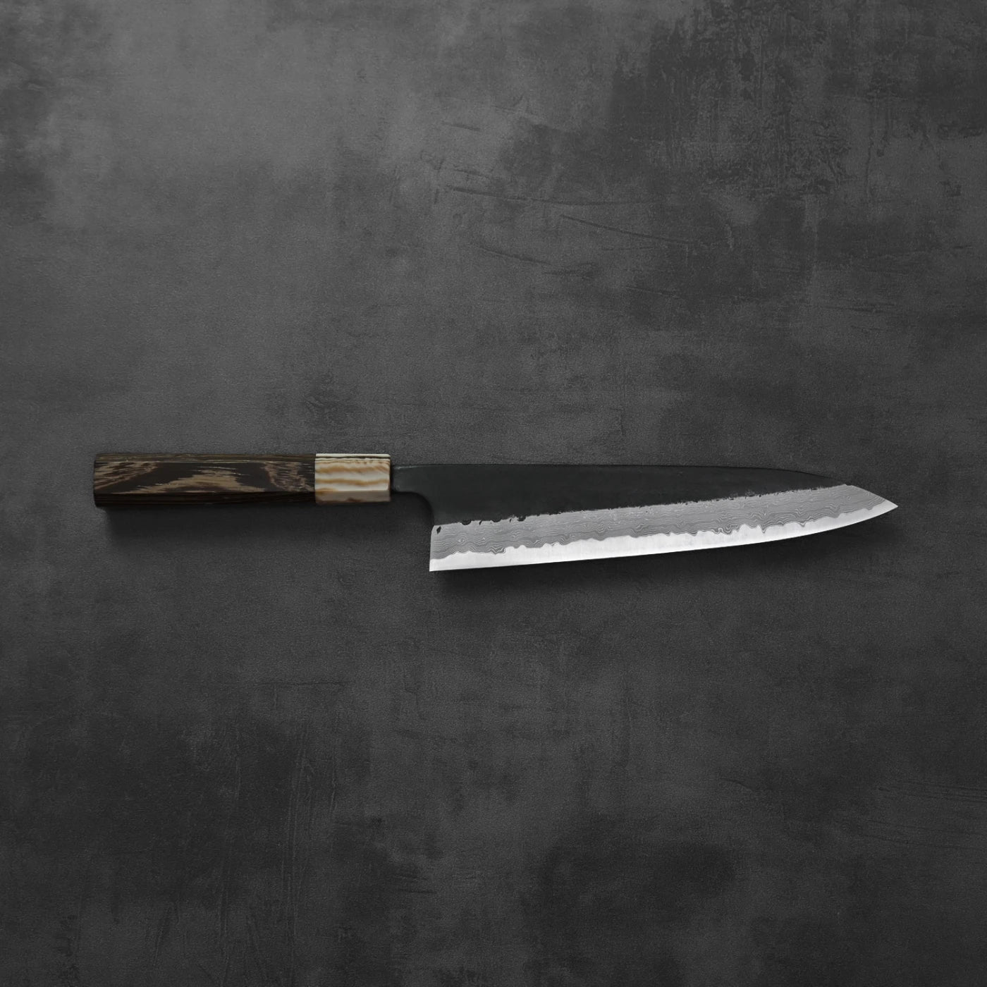 Gyuto with a dark wood handle and damascus pattern along the blade.