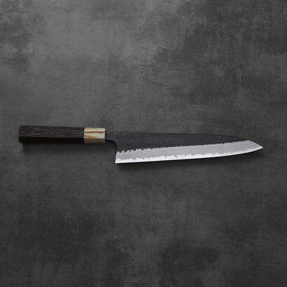 A gyuto knife with a kurouchi damascus finish rests, highlighting its blade and overall silhouette.