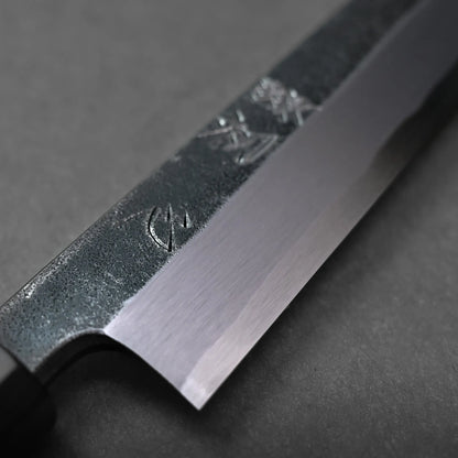 Close-up of a Japanese knife blade featuring distinct kanji engravings and a polished edge, set against a dark, textured surface.