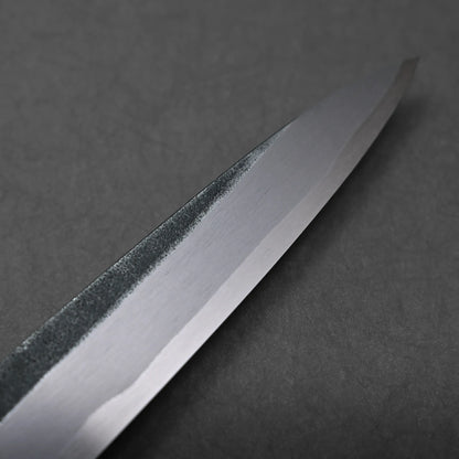 A close-up view of the tip of a shiny kitchen knife resting on a dark, textured surface. The blade’s gleaming finish contrasts with the background for a striking visual effect.
