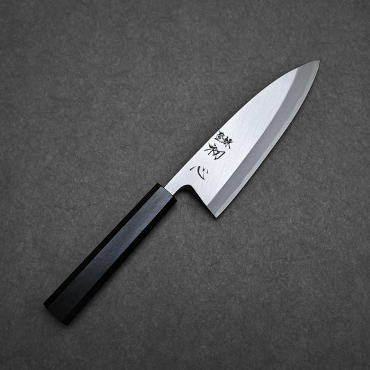 A Hatsukokoro Shirasagi shirogami#2 deba 165mm with a wooden handle and engraved carbon steel blade rests on a dark gray textured surface.