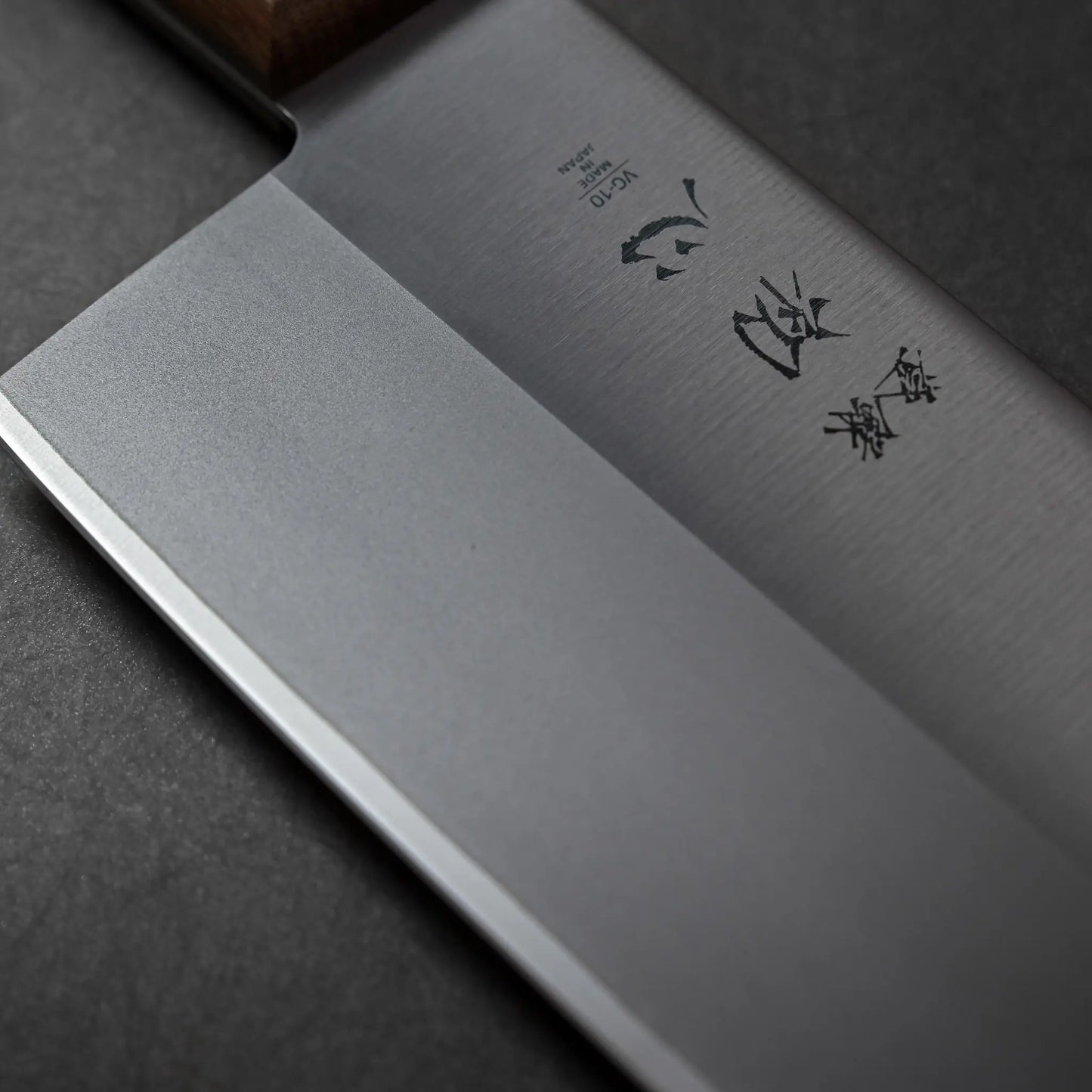 Close-up shows a Japanese knife with a broad, rectangular blade and engraved characters on the VG10 steel surface.