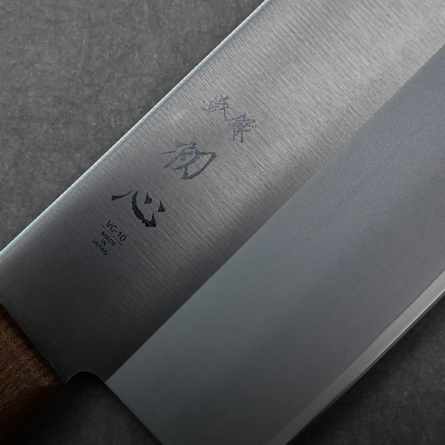 Close-up shows kanji characters on the blade and a wooden handle of this Japanese knife, a chuka bocho cleaver.