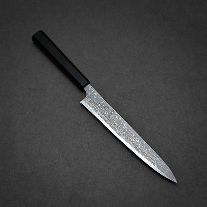 A Japanese-style damascus sashimi knife with a black handle and a patterned, narrow, pointed blade, placed on a dark grey surface.