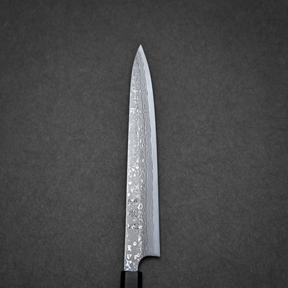 A close-up of a damascus yanagiba with a patterned Damascus steel blade, shown against a dark grey textured background.