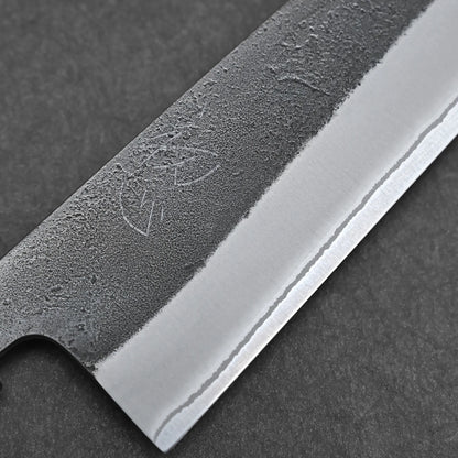 Close-up of a Hatsukokoro x Yoshikane kurouchi nashiji shirogami#2 gyuto 210mm blade, showing its textured matte finish and polished edge with faint etching against a dark background.
