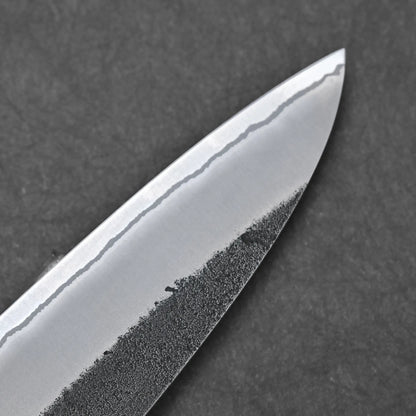 Close-up of the Hatsukokoro x Yoshikane kurouchi nashiji shirogami#2 gyuto 210mm tip, showing its wavy hamon and textured dark lower blade against a dark background.