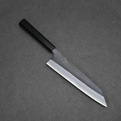 A Hatsukokoro x Yoshikane kurouchi nashiji shirogami#2 kiritsuke gyuto 210mm with a black handle and sharp, angular blade rests on a dark gray surface.
