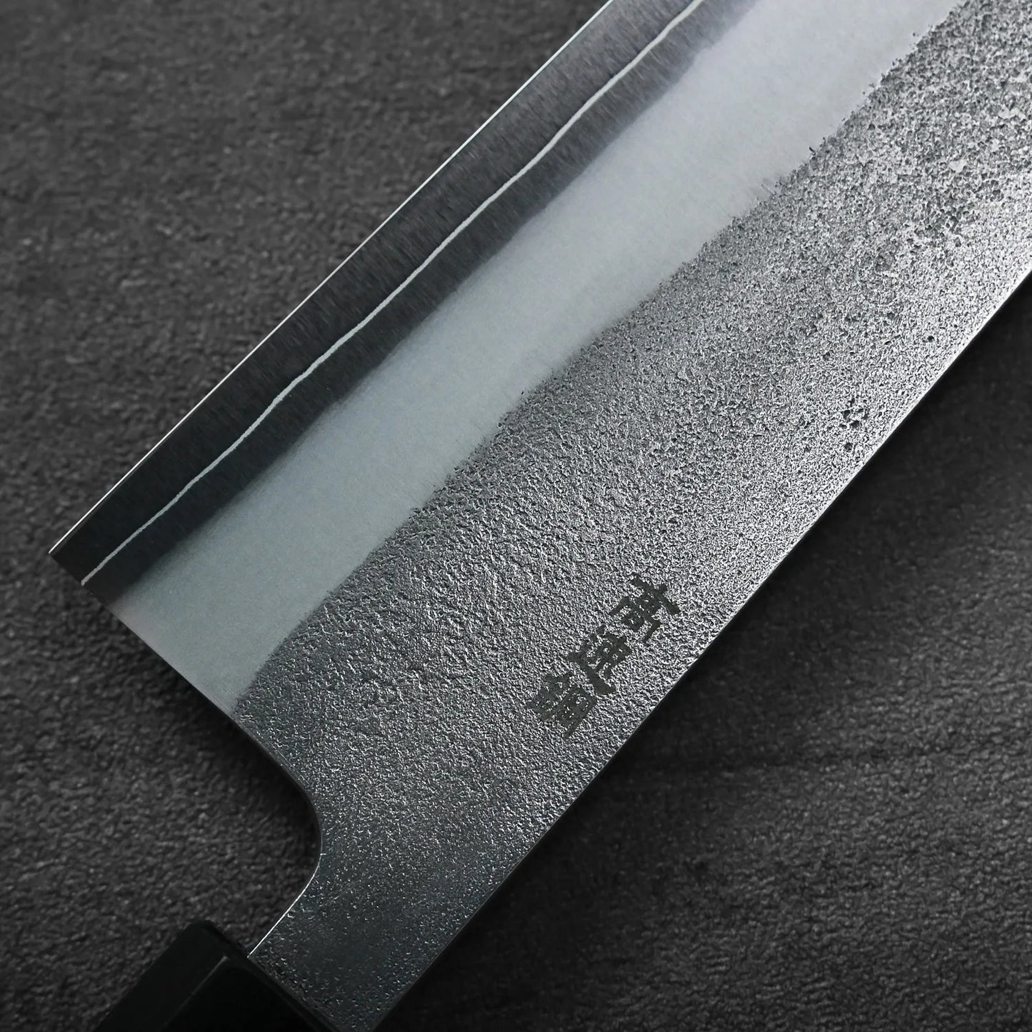 Close-up of a gyuto blade, highlighting its polished and textured steel with distinct visual patterns.