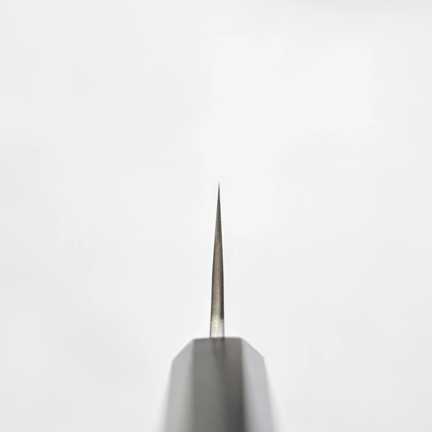 Close-up of the pointed tip of a gyuto, showing its blade shape and metal texture in fine detail.