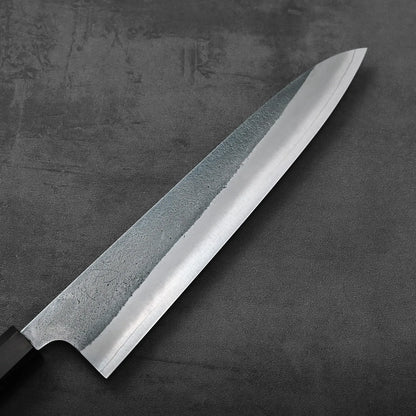 A close-up of a gyuto knife blade, highlighting its nashiji texture and metallic finish.
