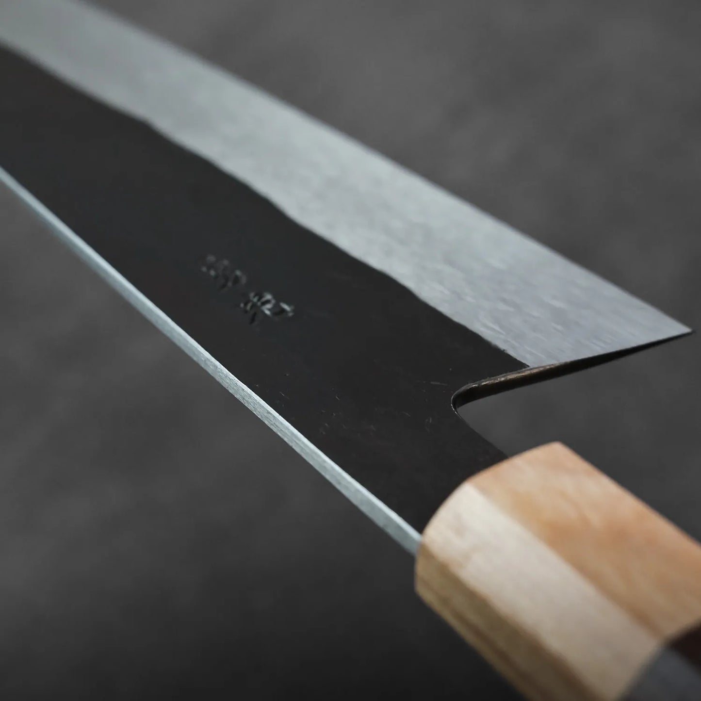 Close-up of gyuto with wood handle and steel blade, highlighting details in the knife’s construction.