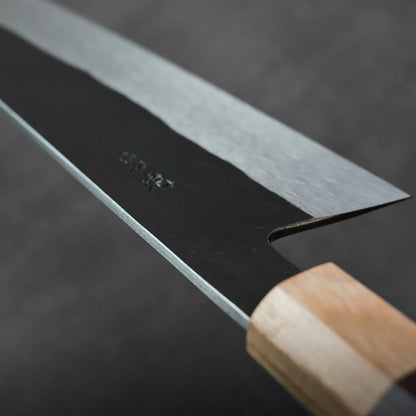 Close-up of gyuto with wood handle and steel blade, highlighting details in the knife’s construction.